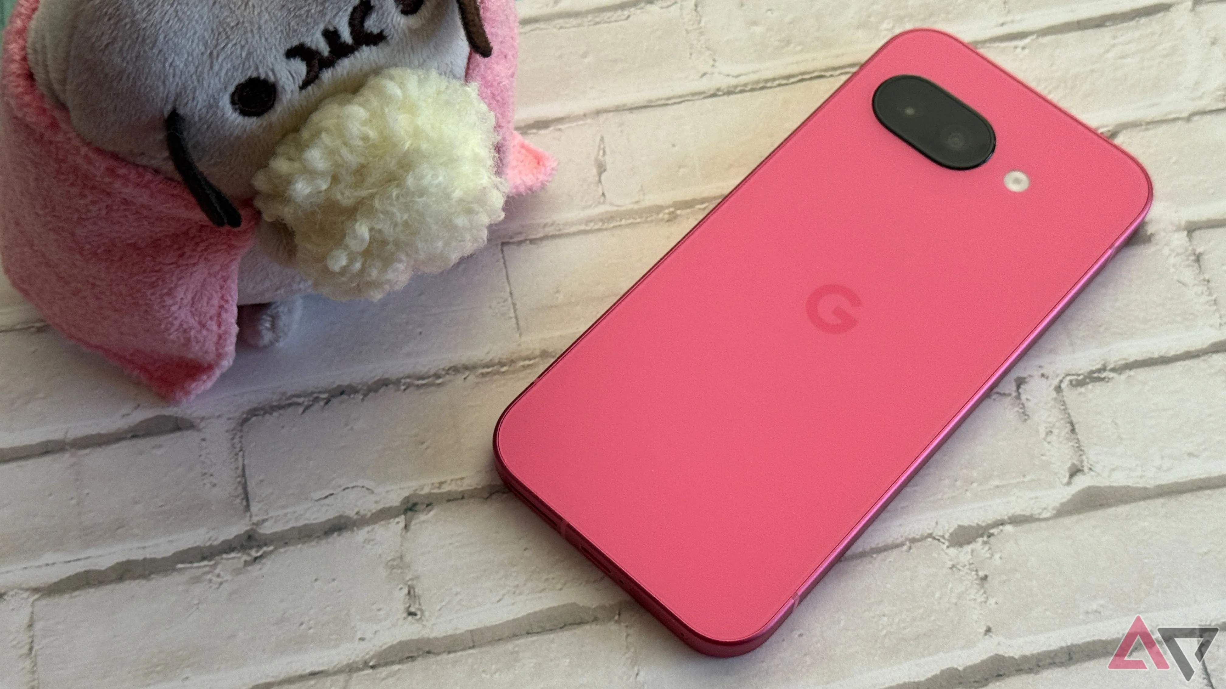 Google Pixel 9a màu Peony (Hồng nhạt) đặt cạnh thú nhồi bông Pusheen