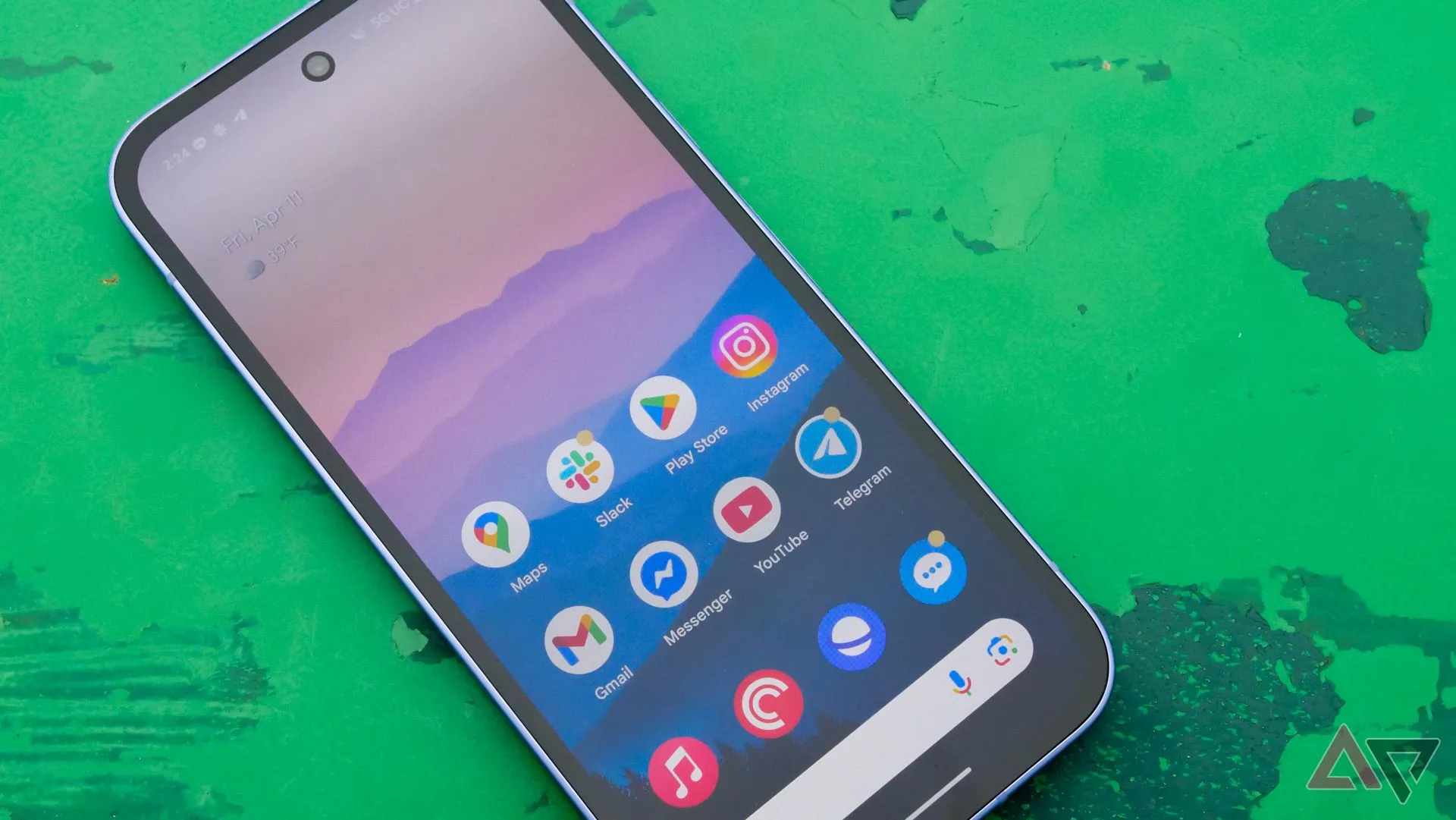 Màn hình Google Pixel 9a hiển thị ngoài trời, đặt trên bàn màu xanh lá cây trong công viên.