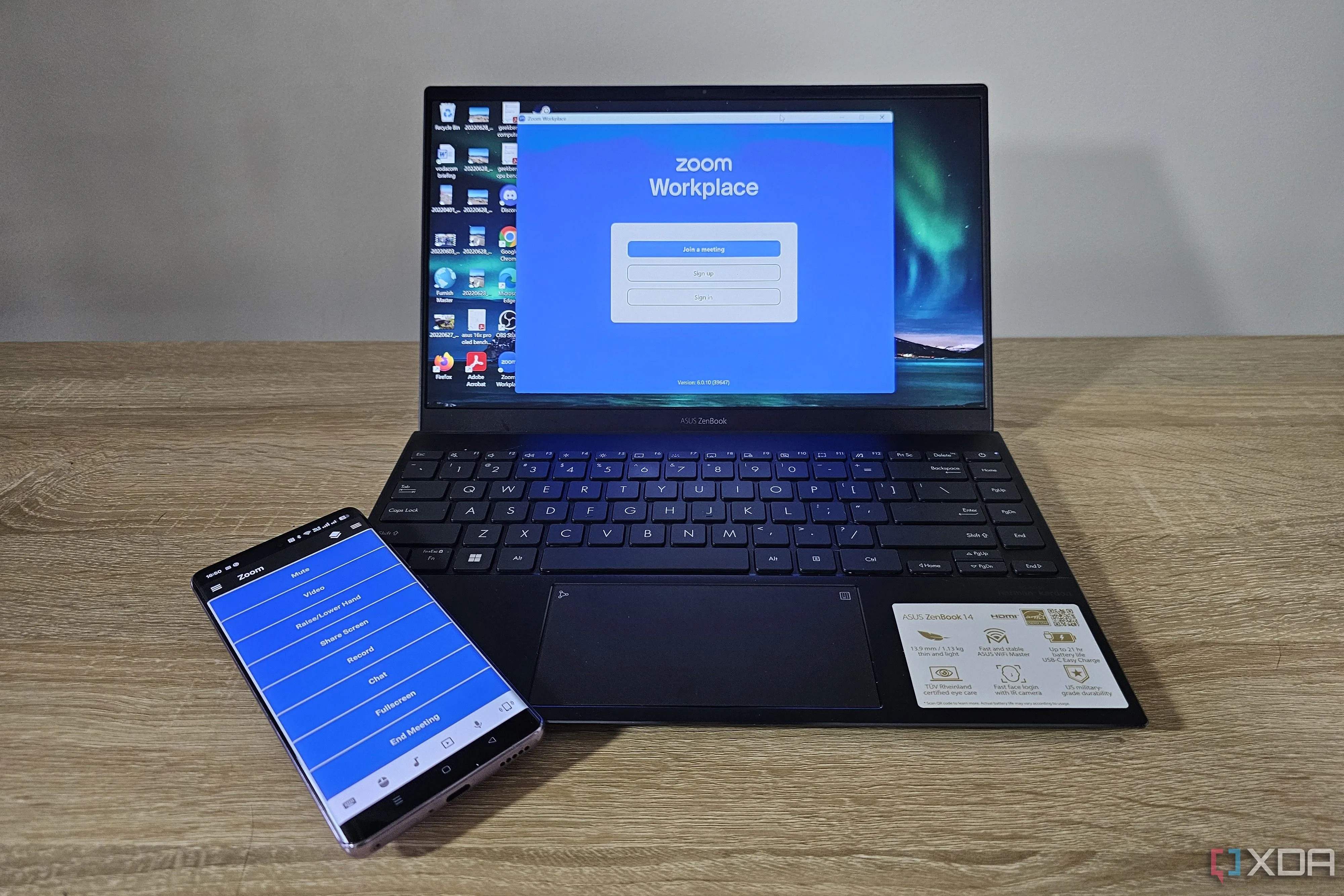 Điện thoại thông minh chạy ứng dụng điều khiển từ xa cạnh laptop đang hiển thị cuộc họp Zoom.