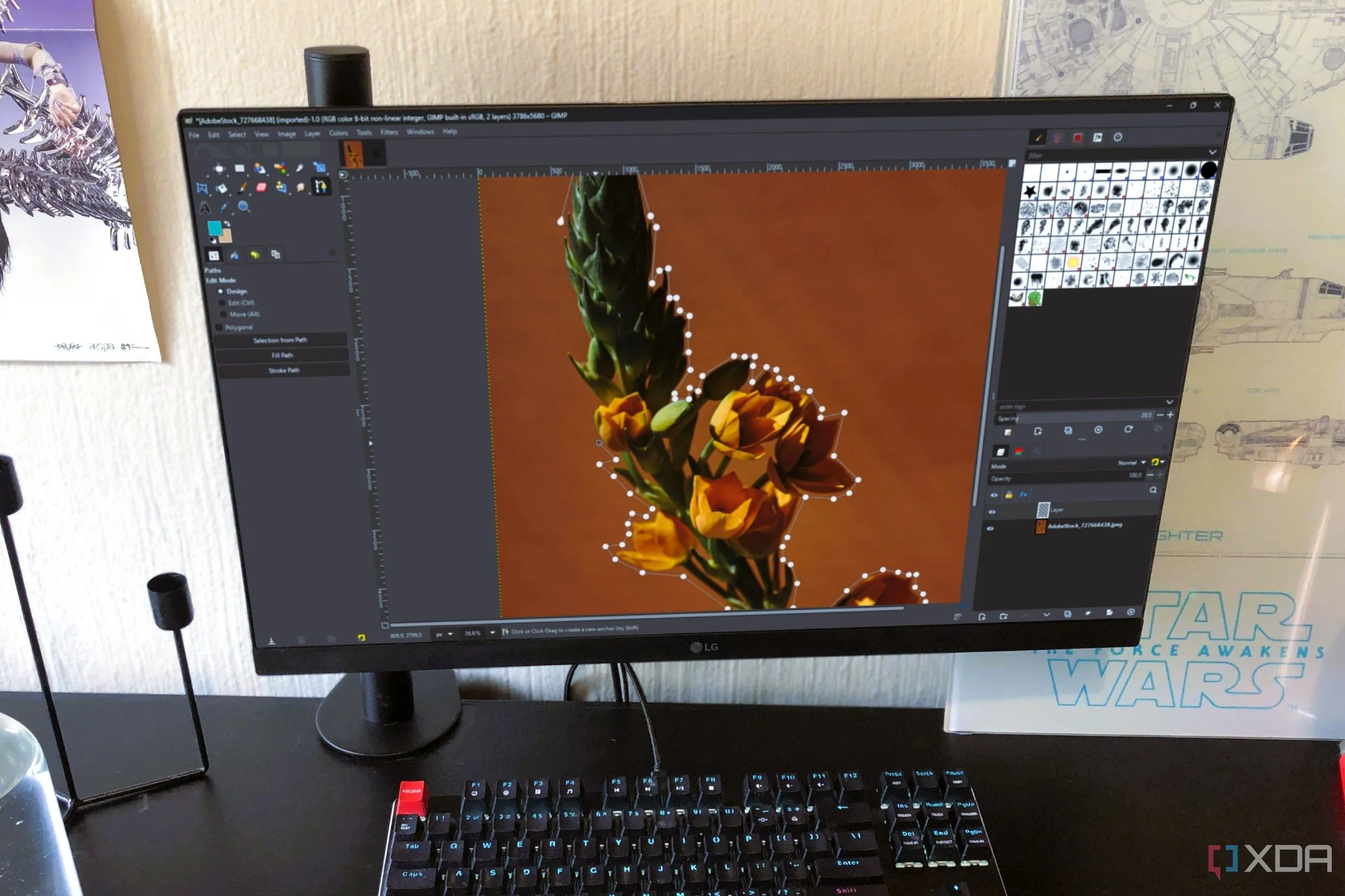 Giao diện chỉnh sửa của GIMP trên màn hình máy tính, cùng với chai nước, chân nến và poster, gợi ý không gian làm việc sáng tạo