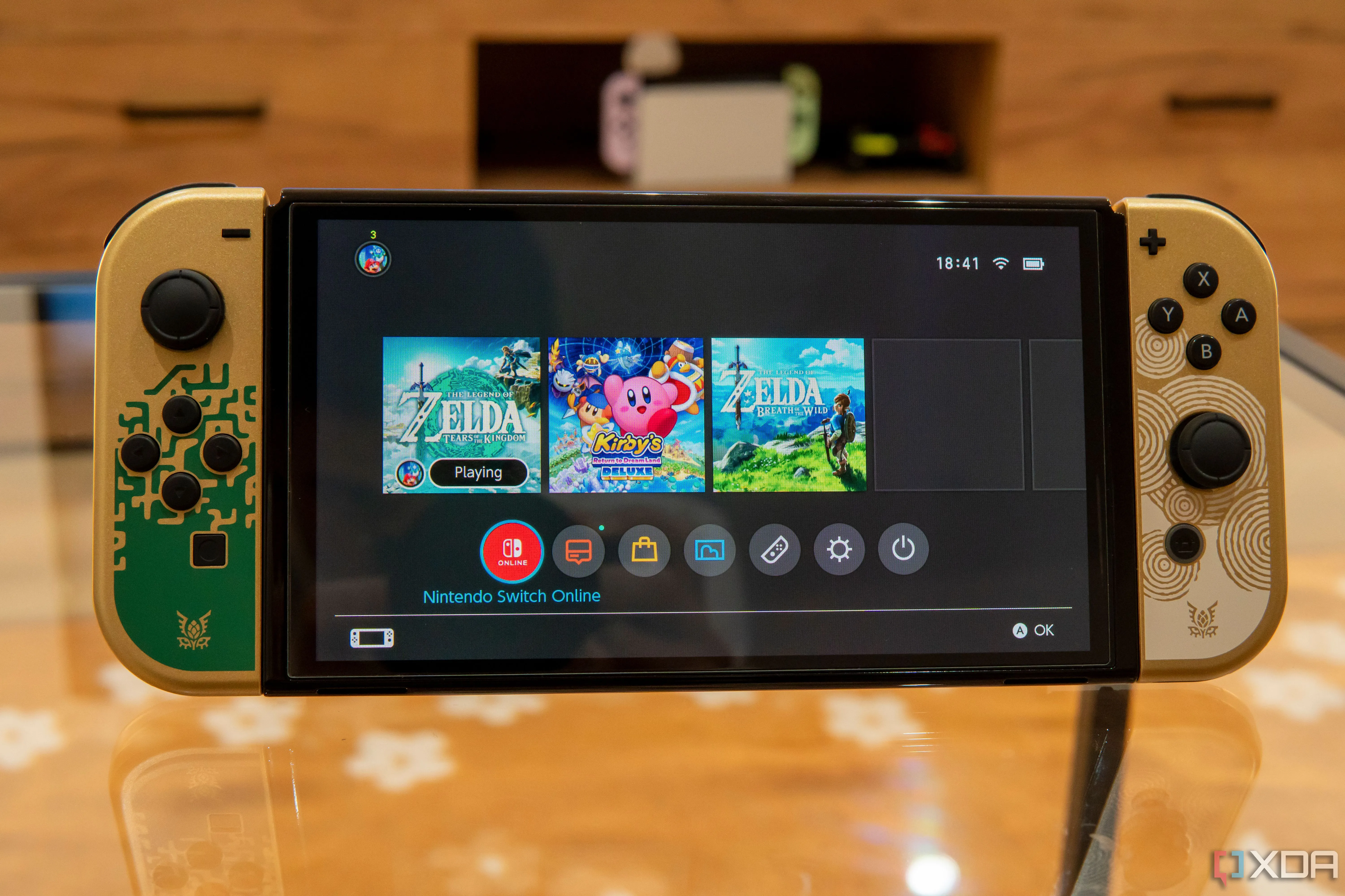 Mô hình Nintendo Switch OLED màu trắng với màn hình hiển thị menu chính và một game đang chạy nền, minh họa cho các tựa game sắp có trên Switch 2.