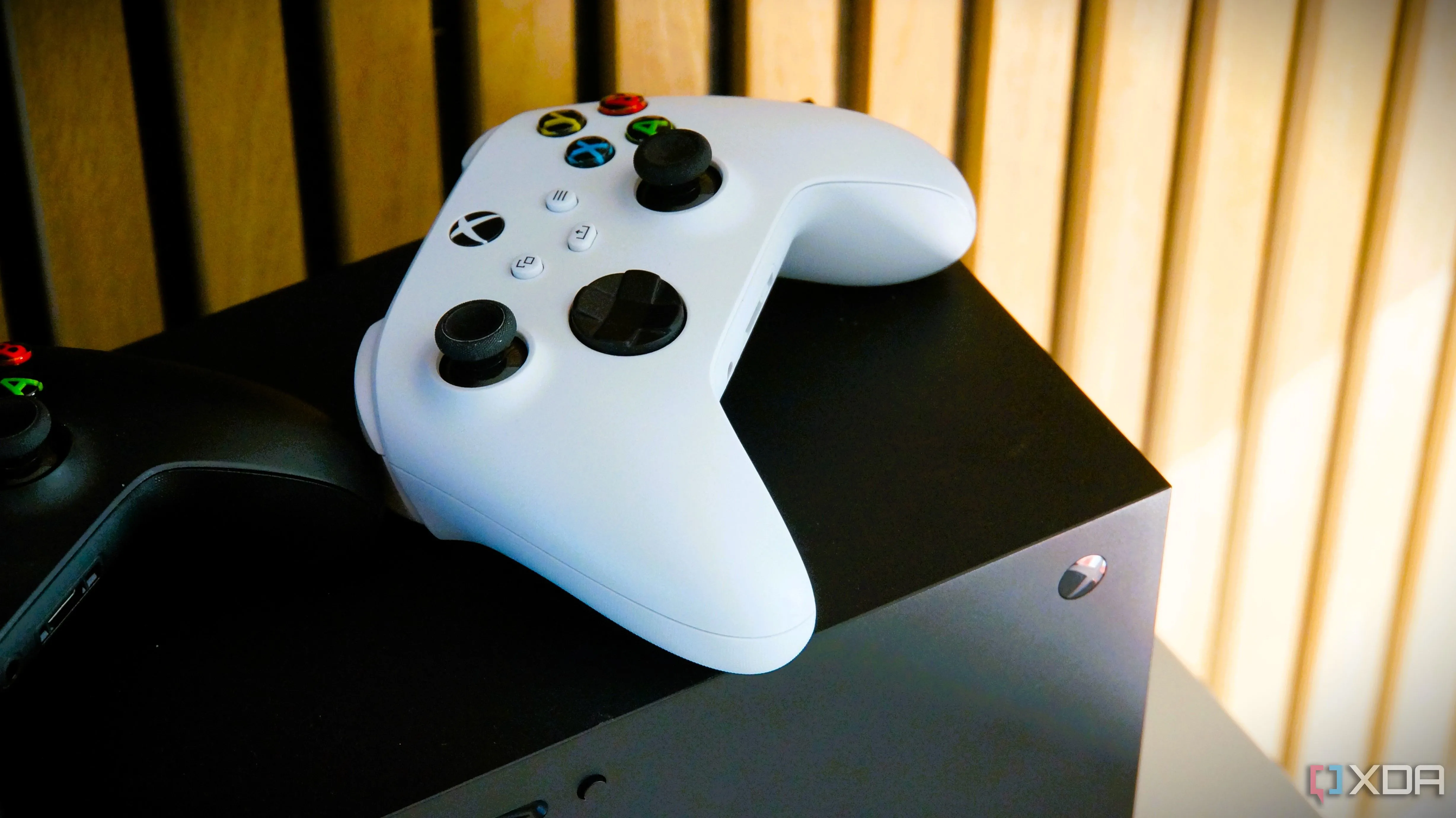 Một bộ điều khiển Xbox màu trắng đặt trên đầu máy console Xbox Series X màu đen, minh họa sự đối lập giữa console và PC.