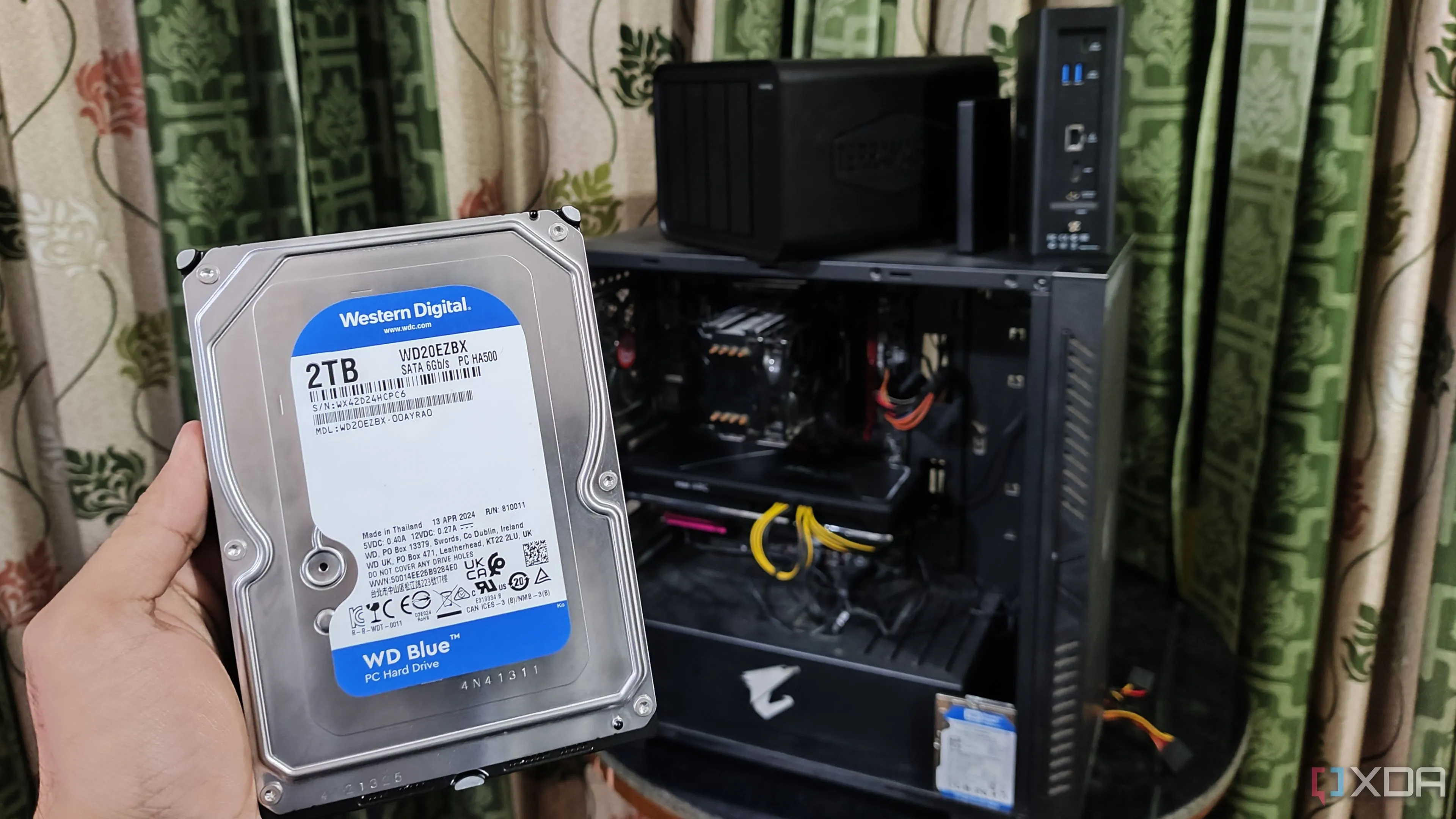 Người dùng cầm ổ cứng HDD trước máy tính và hai thiết bị NAS TerraMaster, minh họa sự so sánh chi phí giữa các giải pháp lưu trữ