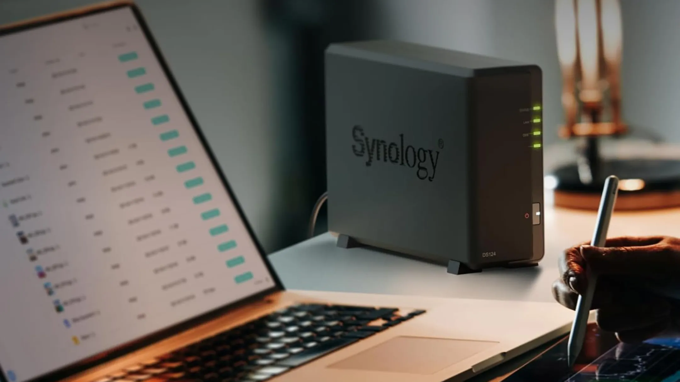 Synology DS124 đặt cạnh laptop trên bàn làm việc, minh họa môi trường sử dụng