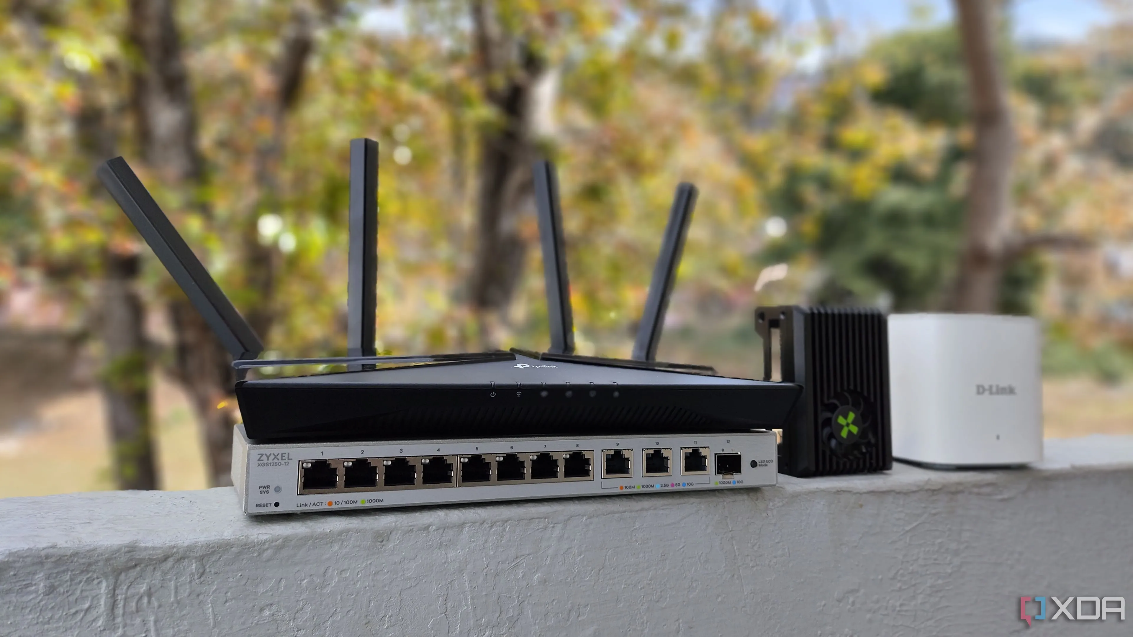 Thiết bị mạng bao gồm bộ định tuyến TP-Link, máy tính bo mạch đơn Radxa X4 SBC, bộ định tuyến D-Link mesh và switch Zyxel, minh họa cho hạ tầng mạng có thể bị tấn công DDoS